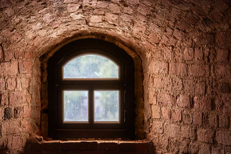 Brown window with an arch in a recess in the wall made of old red brick. From the window of the...