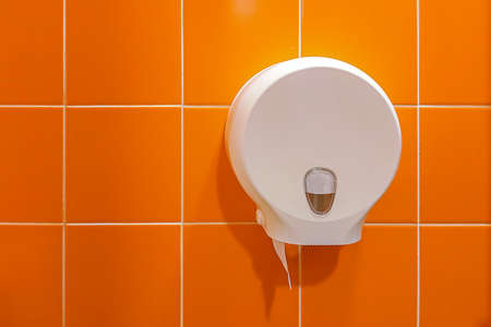 Toilet room interior with toilet paper holder against an orange tile wall.の写真素材