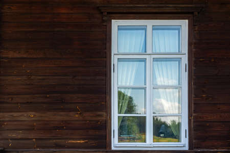 Rectangular window with a white frame against a wall of dark brown wooden planks. From the window of...