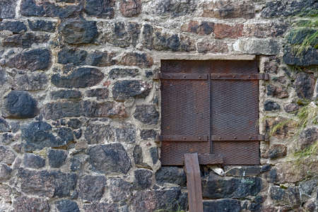 Rectangular window closed with reinforced iron sheet shutters on the stone wall of the old town...