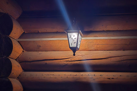 Street lamp hanging on the wall brightly illuminates the red painted logs of the tree in the late evening.の写真素材