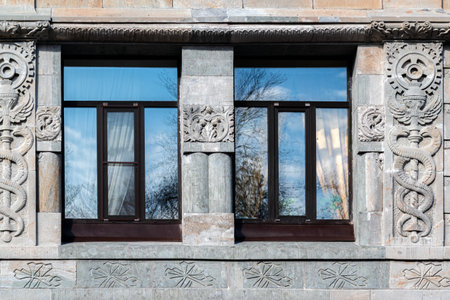 Two rectangular windows with brown frames against a wall of gray blocks with an ornament. From the Windows of the World series.の写真素材