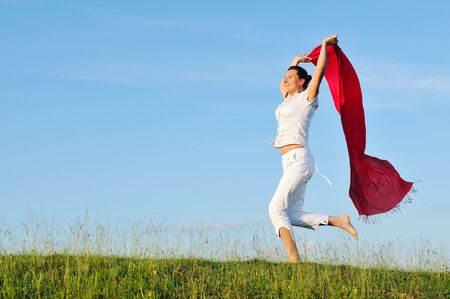 beautiful young and healthy woman run and jump on meadow at sunny day with red scarfの写真素材