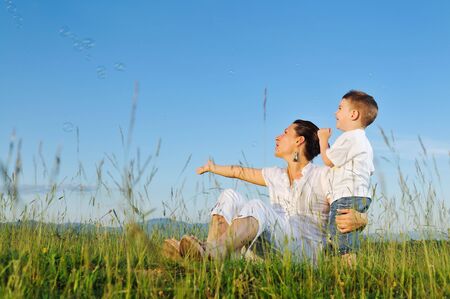 happy child and woman outdoor playing with soap bubble on meadowの写真素材