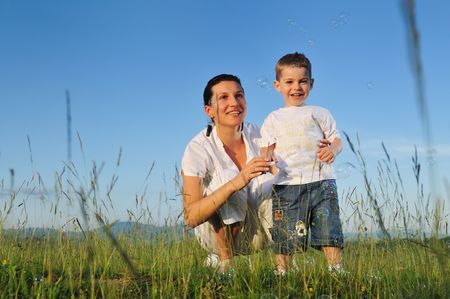 happy child and woman outdoor playing with soap bubble on meadowの写真素材