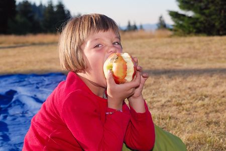cute little girl eating apple in natureの写真素材
