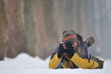 pro photographer with yellow jacket lie on snow and making shoot