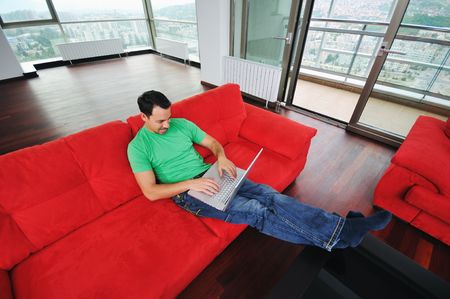 young man relax on red sofa and work on laptop at home indoor の写真素材