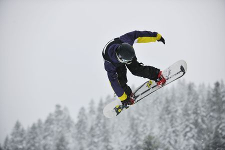 young boys jumping in air ind showing trick with snowboard at winter season