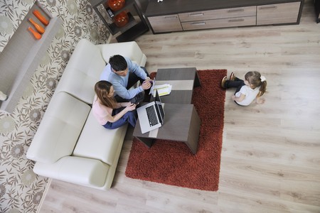young happy family at bright and modern living room puting money in piggy bank and working on laptop computer on home financeの写真素材
