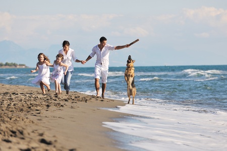 happy young family in white clothing have fun and play with beautiful dog at vacations on beautiful beachの写真素材