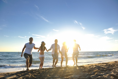 happy young friends group have fun and celebrate while jumping and running on the beach at the sunsetの写真素材