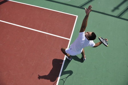 young man play tennis outdoor on orange tennis court at early morningの写真素材