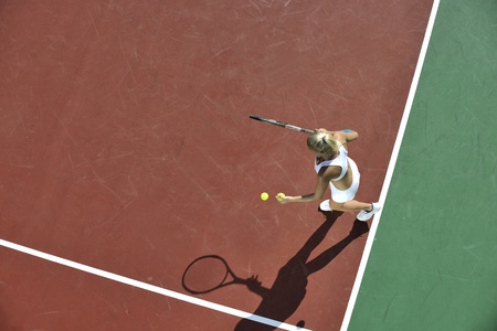 young fit woman play tennis outdoor on orange tennis field at early morningの写真素材