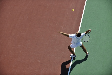 young man play tennis outdoor on orange tennis field at early morningの写真素材