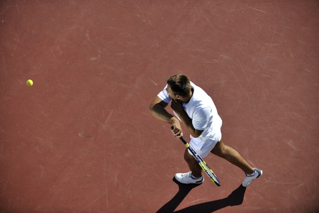 young man play tennis outdoor on orange tennis field at early morningの写真素材