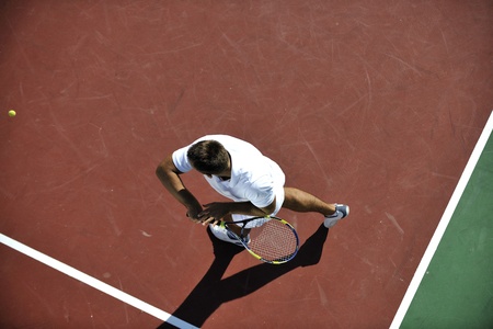 young man play tennis outdoor on orange tennis field at early morningの写真素材