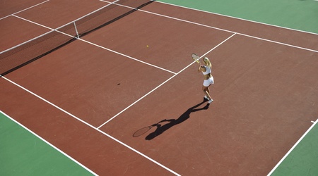 young fit woman play tennis outdoor on orange tennis field at early morningの写真素材