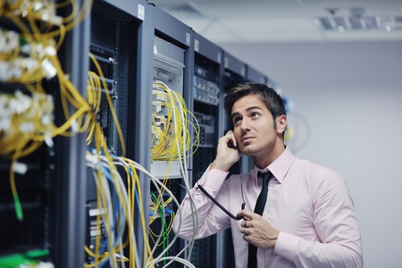 young business man computer science engeneer talking by cellphone at network datacenter server room asking  for help and fast solutions and servicesの写真素材