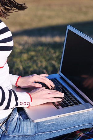 young teen woman work on laptop computer outdoor in nature with blue sky and green grass in backgroundの写真素材