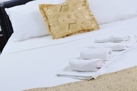 white towels on bed in luxury hotel room with yellow pillow in backgroundの写真素材