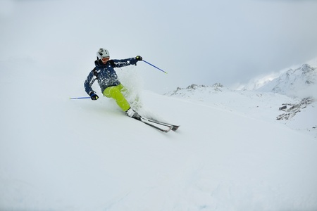 skier skiing downhill on fresh powder snow  with sun and mountains in background