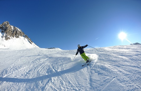 skier skiing downhill on fresh powder snow  with sun and mountains in backgroundの写真素材