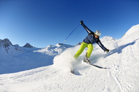 skier skiing downhill on fresh powder snow  with sun and mountains in background