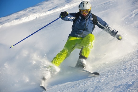 skier skiing downhill on fresh powder snow  with sun and mountains in backgroundの写真素材