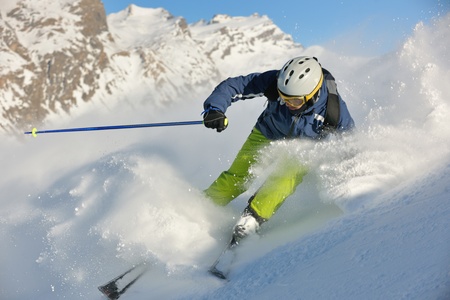 skier skiing downhill on fresh powder snow  with sun and mountains in backgroundの写真素材