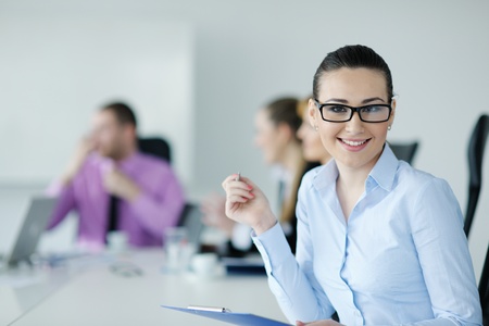 Successful business woman standing with her staff in background at modern bright office
