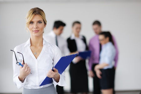 Successful business woman standing with her staff in background at modern bright officeの写真素材