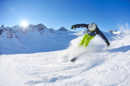 skier skiing downhill on fresh powder snow  with sun and mountains in backgroundのeditorial素材
