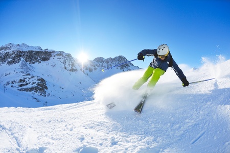 skier skiing downhill on fresh powder snow with sun and mountains in background skier skiing downhill on fresh powder snow with sun and mountains in background