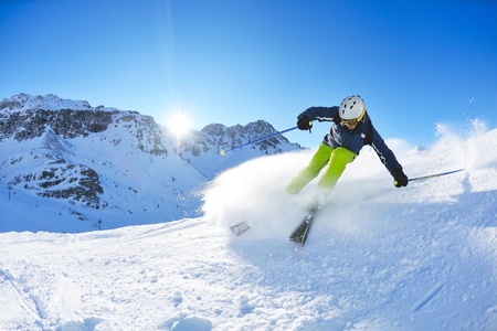 skier skiing downhill on fresh powder snow  with sun and mountains in backgroundの写真素材