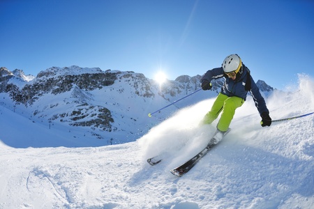 skier skiing downhill on fresh powder snow  with sun and mountains in backgroundのeditorial素材