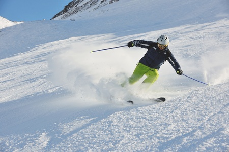 skier skiing downhill on fresh powder snow  with sun and mountains in backgroundのeditorial素材