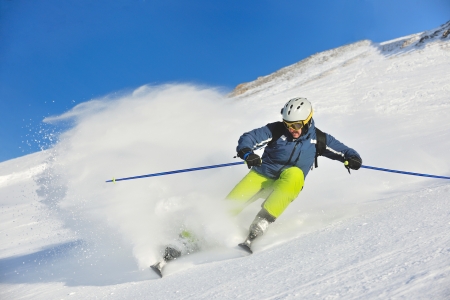 skier skiing downhill on fresh powder snow  with sun and mountains in backgroundのeditorial素材