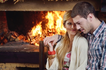 happy Young romantic couple and relaxing sofa in front of fireplace at winter season in homeの写真素材