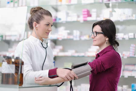 doctor checking blood pressure and heart rate in a hospital or in pharmacy with young female patientの写真素材