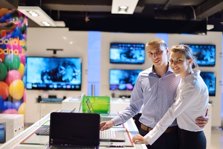 Young couple in consumer electronics store looking at latest laptop, television and photo camera to buyの写真素材