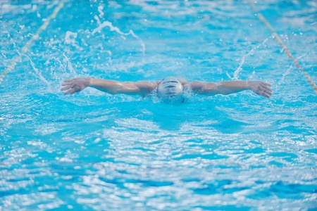 Happy muscular swimmer wearing glasses and cap at swimming pool and represent health and fit concept