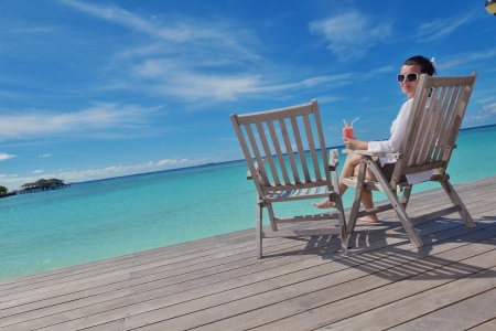 Beautiful young woman in bikini lying on a deckchair with a drink by the seaの写真素材