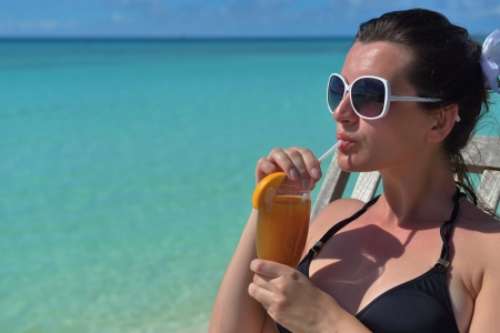Beautiful young woman in bikini lying on a deckchair with a drink by the seaの写真素材