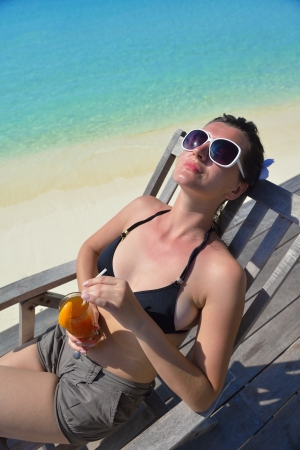 Beautiful young woman in bikini lying on a deckchair with a drink by the seaの写真素材