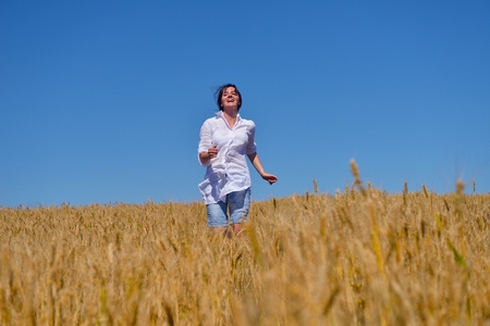 Young woman standing jumping and running  on a wheat field with blue sky the background at summer day representing healthy life and agriculture conceptの写真素材