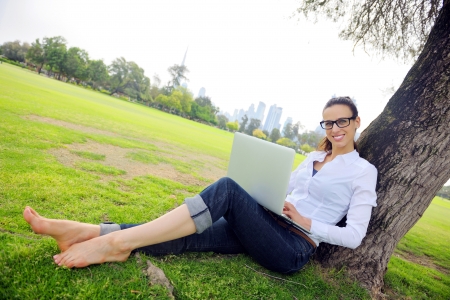 happy young student woman with laptop in city park studyの写真素材