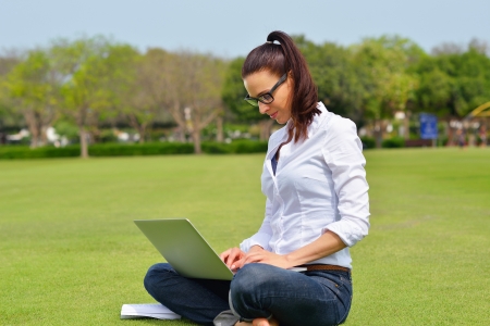happy young student woman with laptop in city park studyの写真素材