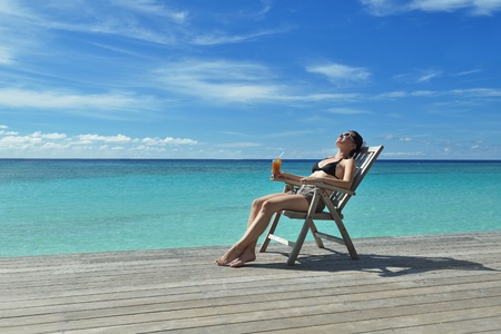 Beautiful young woman in bikini lying on a deckchair with a drink by the seaの写真素材