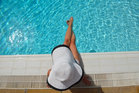 Happy smiling woman with hat and sunglasses  in swimming pool at tropical resort